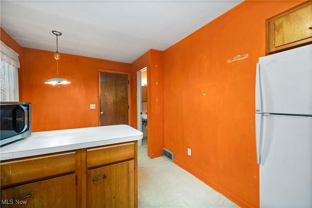 kitchen featuring freestanding refrigerator, stainless steel microwave, light carpet, and brown cabinets
