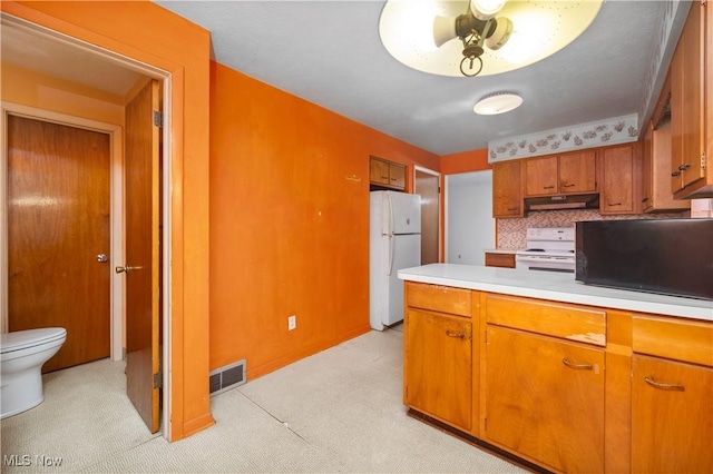 kitchen with white appliances, under cabinet range hood, light countertops, brown cabinetry, and light carpet