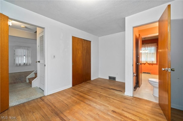 unfurnished bedroom featuring hardwood / wood-style floors, ensuite bathroom, a textured ceiling, a baseboard heating unit, and baseboards