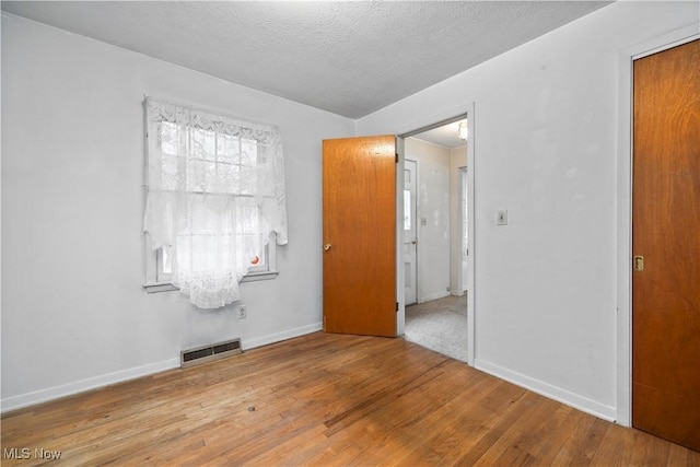 spare room featuring wood finished floors, baseboards, and a textured ceiling