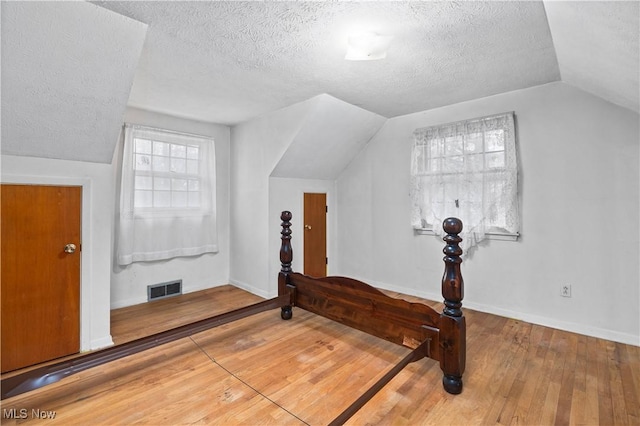 bonus room with lofted ceiling, a textured ceiling, hardwood / wood-style flooring, and baseboards