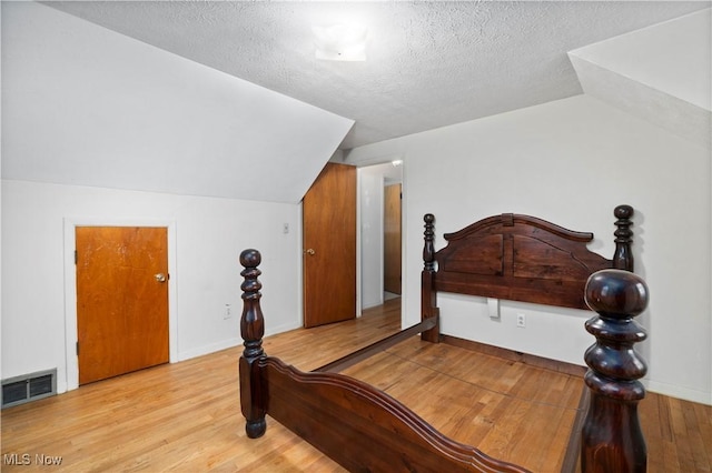 bedroom with vaulted ceiling, a textured ceiling, and light wood finished floors