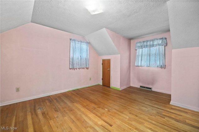 bonus room featuring lofted ceiling, wood-type flooring, a textured ceiling, and baseboards
