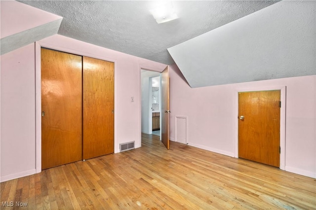 additional living space featuring hardwood / wood-style floors, lofted ceiling, a textured ceiling, and baseboards