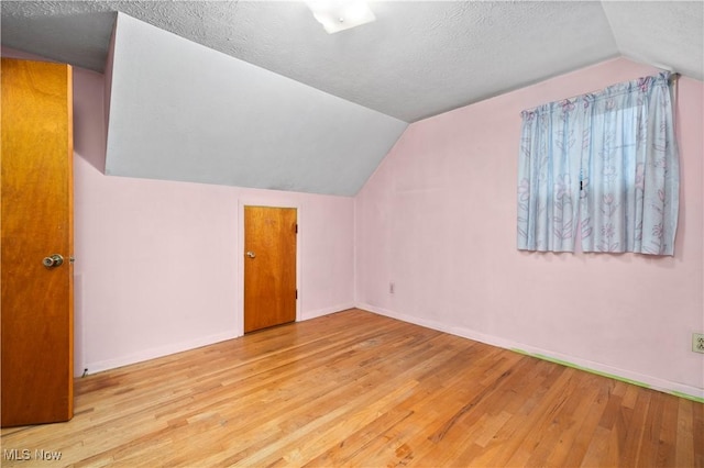 additional living space featuring lofted ceiling, wood finished floors, baseboards, and a textured ceiling