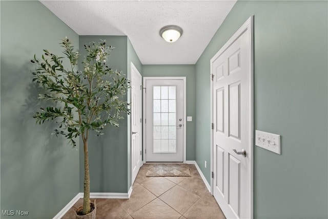doorway to outside with a textured ceiling, baseboards, and light tile patterned flooring