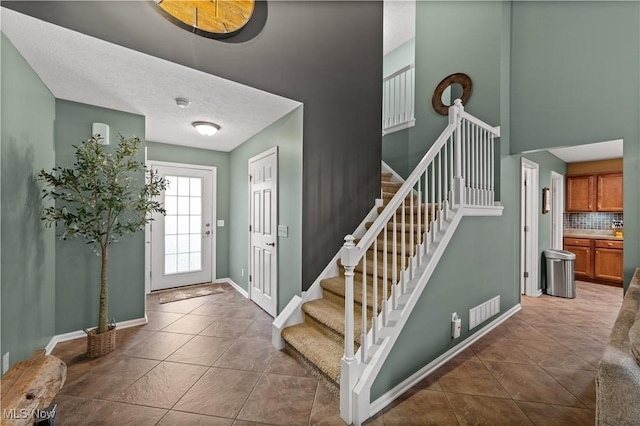 tiled entrance foyer with baseboards, stairway, and a towering ceiling