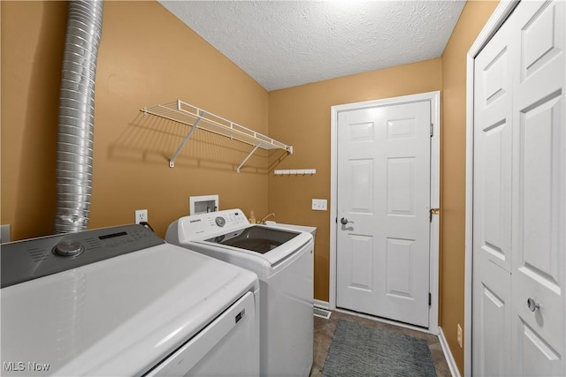 clothes washing area with washer and dryer, baseboards, and a textured ceiling