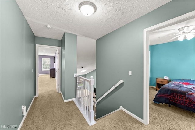 hallway with an upstairs landing, carpet, baseboards, and a textured ceiling