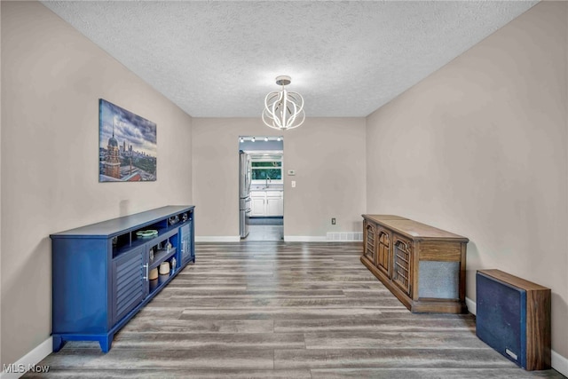 unfurnished dining area with wood finished floors, a chandelier, baseboards, and a textured ceiling