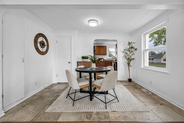 dining area featuring arched walkways, stone finish floors, and baseboards