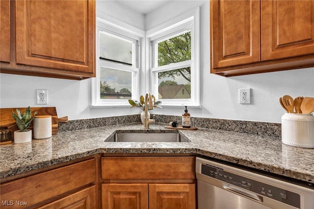 kitchen featuring dishwasher, a sink, dark stone counters, and brown cabinets