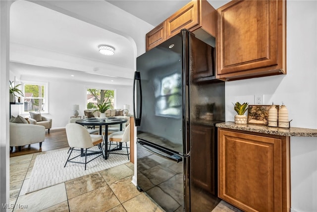 kitchen featuring freestanding refrigerator, light stone countertops, and brown cabinetry