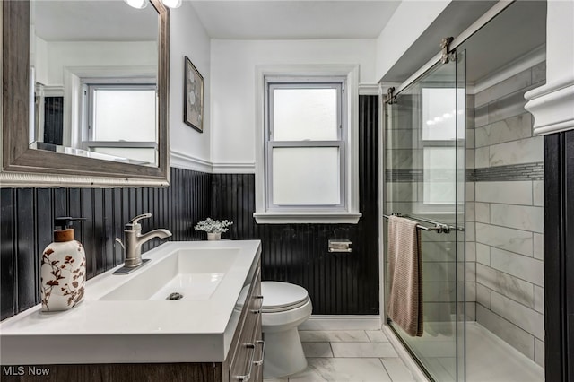 bathroom with marble finish flooring, a stall shower, a wainscoted wall, toilet, and vanity