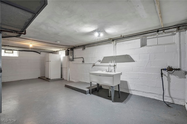 below grade area with freestanding refrigerator, concrete block wall, a sink, and electric panel