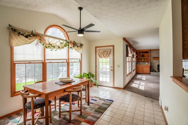 dining room featuring lofted ceiling, healthy amount of natural light, ceiling fan, a fireplace, and light tile patterned floors