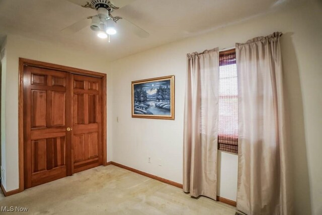 unfurnished bedroom featuring light carpet, baseboards, and a ceiling fan