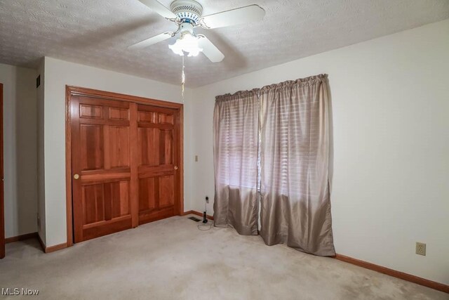 unfurnished bedroom featuring baseboards, carpet floors, a textured ceiling, a ceiling fan, and a closet