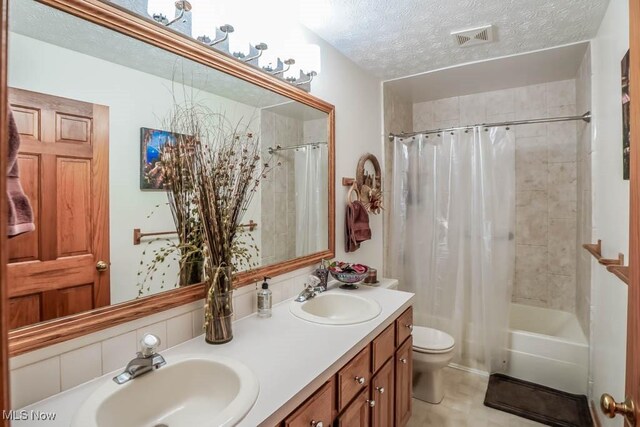 bathroom featuring a textured ceiling, toilet, shower / bathtub combination with curtain, and double vanity