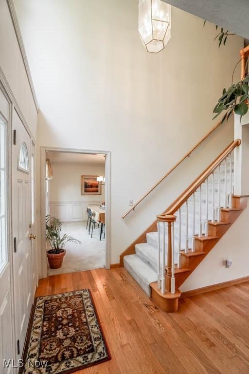 entrance foyer with stairs, wood finished floors, a high ceiling, a chandelier, and baseboards