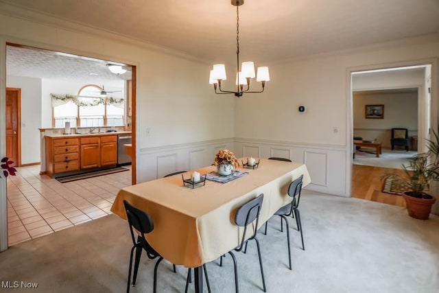 dining space featuring a chandelier, ornamental molding, light colored carpet, and wainscoting