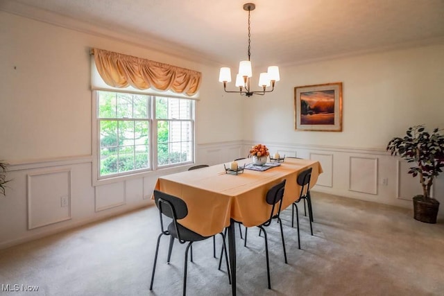 dining room with a chandelier, light colored carpet, a decorative wall, crown molding, and a wainscoted wall