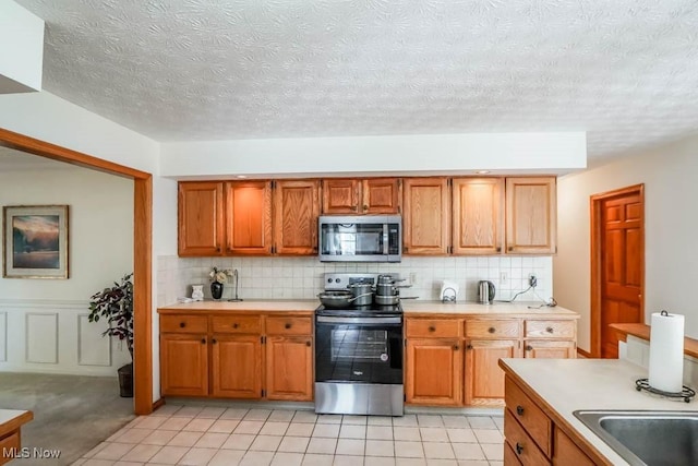 kitchen with stainless steel appliances, light countertops, backsplash, a textured ceiling, and wainscoting