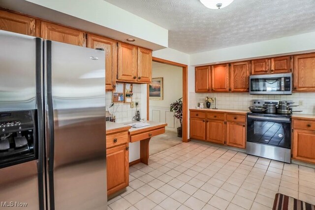 kitchen featuring appliances with stainless steel finishes, light countertops, decorative backsplash, brown cabinets, and a textured ceiling