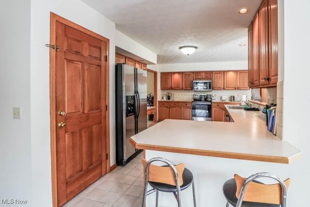 kitchen with stainless steel appliances, a peninsula, light countertops, a sink, and backsplash