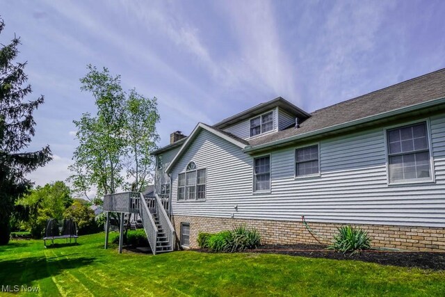 view of home's exterior with a trampoline, stairs, a lawn, a deck, and a chimney
