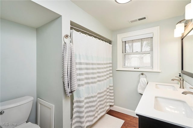 bathroom with wood finished floors, toilet, baseboards, double vanity, and a shower with curtain