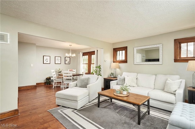 living room featuring wood finished floors, a chandelier, a textured ceiling, healthy amount of natural light, and baseboards