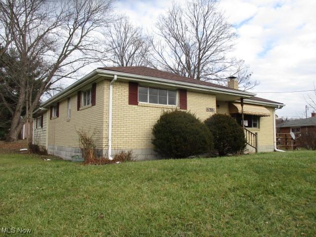 view of side of property featuring a chimney, brick siding, and a yard
