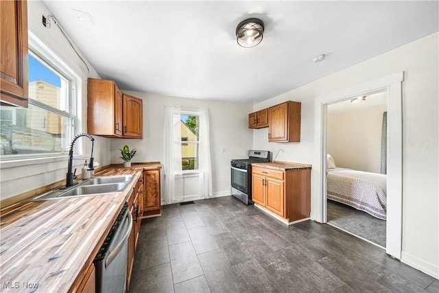 kitchen with appliances with stainless steel finishes, a sink, brown cabinets, wood counters, and baseboards