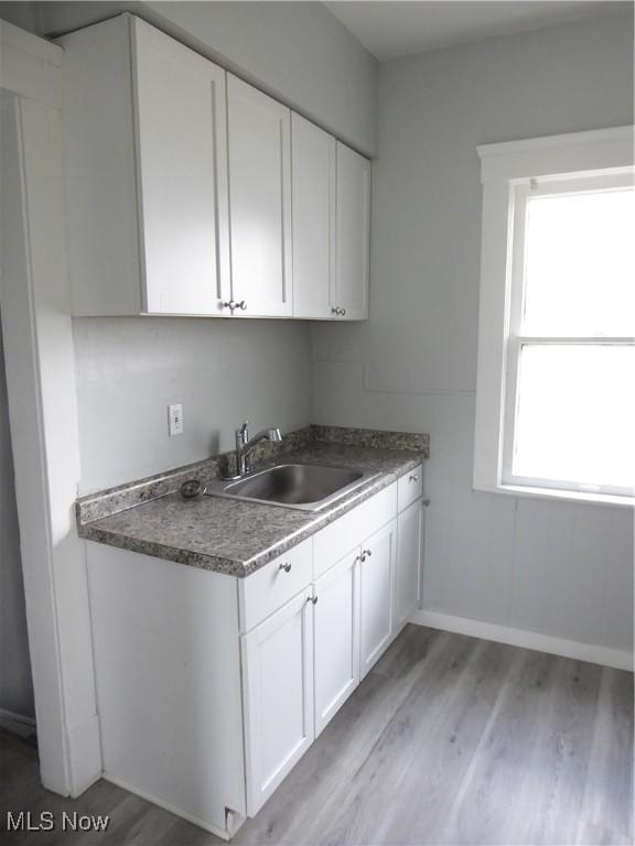 2067 W 105th St, Cleveland, OH 44102 - kitchen with a sink, white cabinetry, light wood-style floors, baseboards, and dark countertops