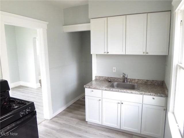 2067 W 105th St, Cleveland, OH 44102 - kitchen featuring black gas range, a sink, light wood finished floors, white cabinets, and baseboards