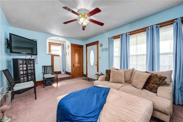 living room with a ceiling fan, carpet floors, arched walkways, baseboards, and a textured ceiling