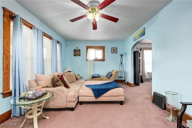 bedroom with a textured ceiling, arched walkways, carpet flooring, baseboards, and ceiling fan