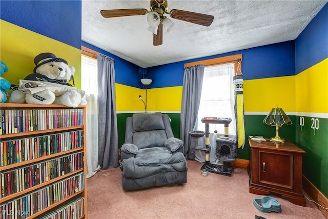 living area featuring plenty of natural light, a textured ceiling, a ceiling fan, carpet, and baseboards