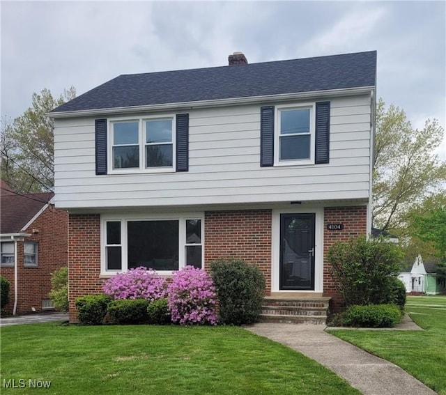 colonial inspired home featuring a front lawn, brick siding, a chimney, and entry steps