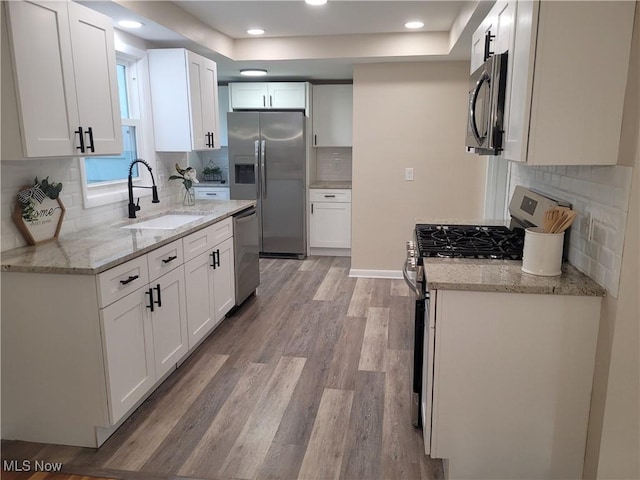kitchen featuring stainless steel appliances, a sink, backsplash, white cabinetry, and light wood finished floors