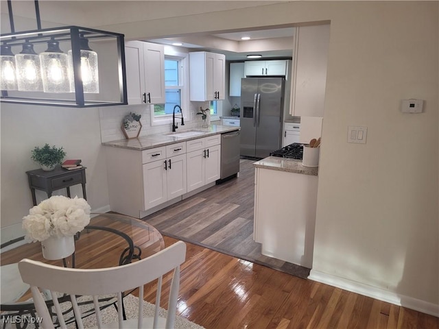 kitchen with appliances with stainless steel finishes, wood finished floors, white cabinets, light stone counters, and tasteful backsplash