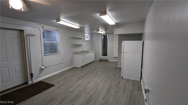 finished below grade area featuring freestanding refrigerator, light wood-style floors, a sink, and baseboards