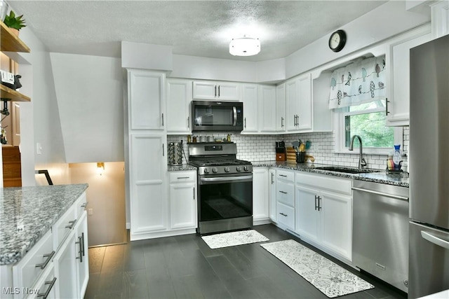 kitchen with appliances with stainless steel finishes, a sink, white cabinets, decorative backsplash, and stone countertops