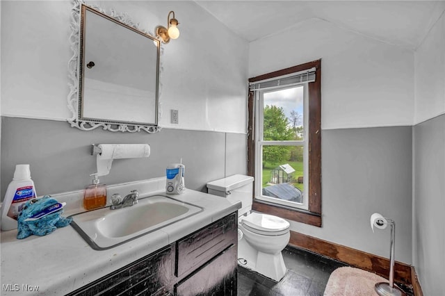 bathroom featuring toilet, vanity, vaulted ceiling, and baseboards