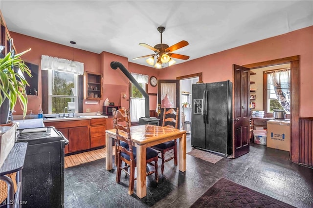 kitchen with black fridge with ice dispenser, stove, brown cabinets, a ceiling fan, and light countertops