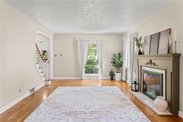 living room featuring a glass covered fireplace, a textured ceiling, wood finished floors, stairs, and baseboards