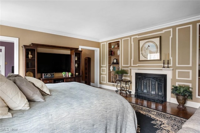 bedroom featuring ornamental molding, a glass covered fireplace, and wood finished floors