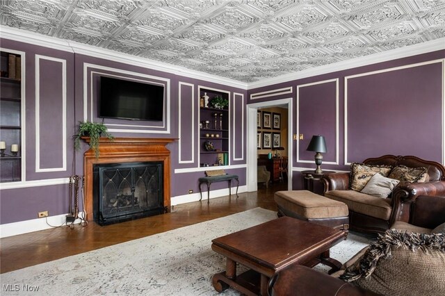 living room featuring a fireplace, built in shelves, an ornate ceiling, baseboards, and wood finished floors