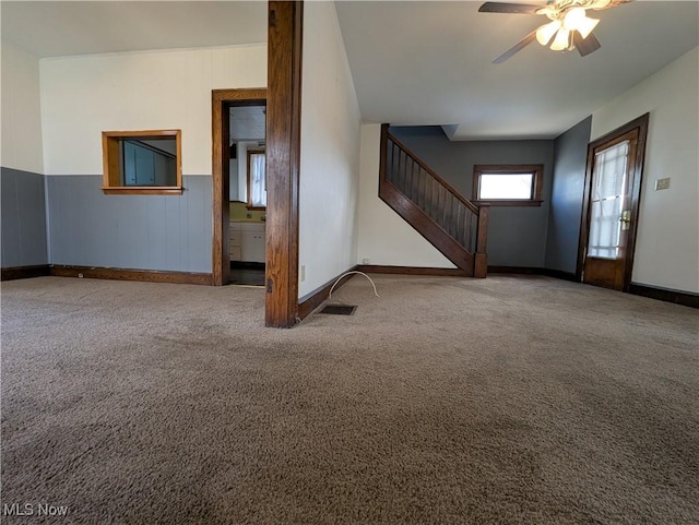 unfurnished living room featuring stairway, a ceiling fan, carpet, and baseboards